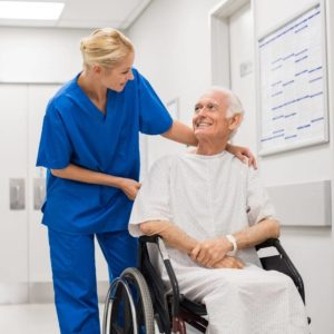 badante che accompagna assistito in sedia a rotelle per una visita dopo un ricovero in ospedale