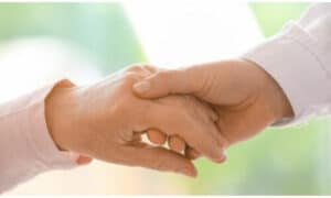 badante che stringe la mano all'anziano che aqssiste in segno di affetto